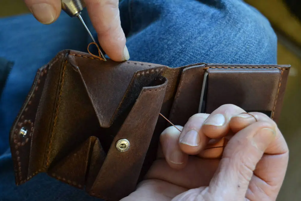 Eine Geldbörse wird von Hand genäht. Das Bild zeigt zwei Hände beim Nähen